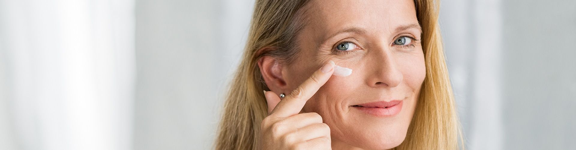 Frau schaut in den Spiegel und cremt sich das Gesicht.